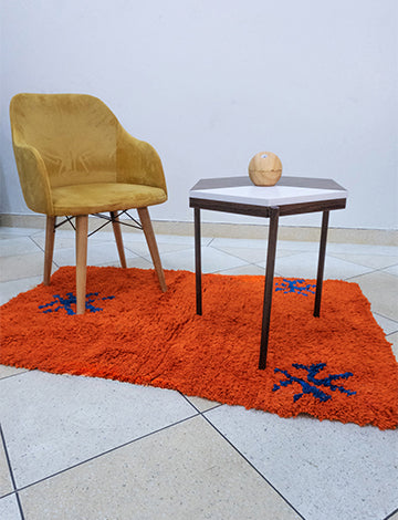 Vibrant orange Berber Moroccan rug with intricate blue Amazigh symbols enhancing a living room decor.